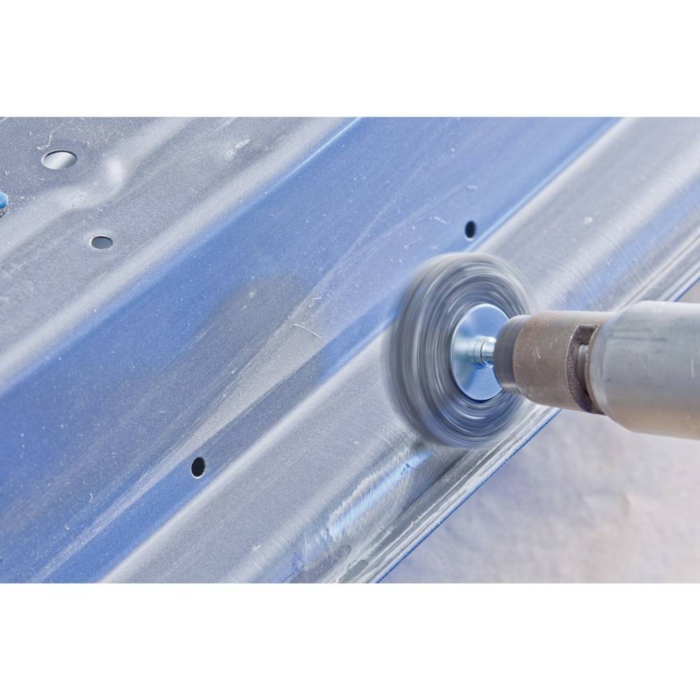 A drill with a polishing attachment is working on a blue metal surface. Dirt is being removed, and the surface is being smoothed.