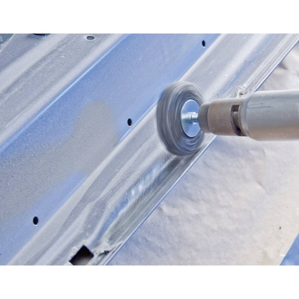 A metal surface is being polished with an electric tool. The tool creates a circular grinding effect on the surface.