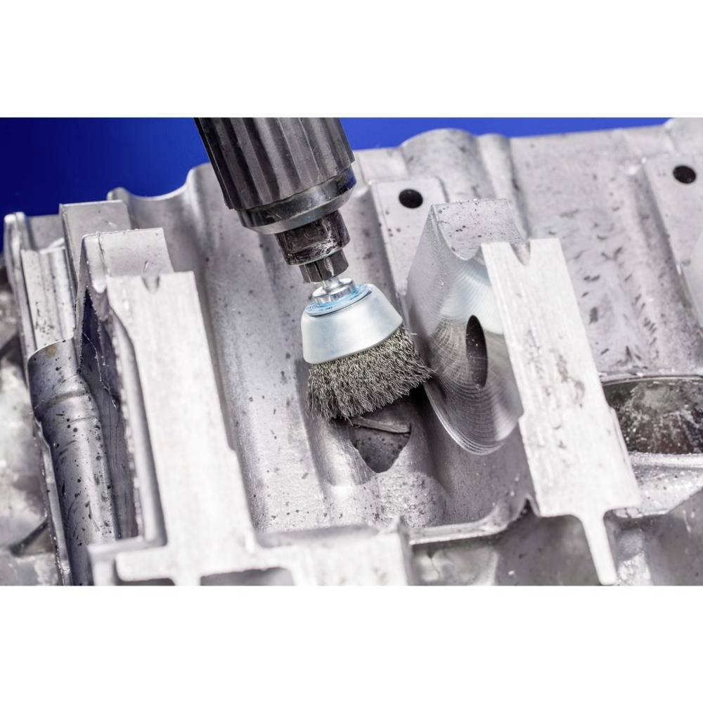 A rotating wire brush grinds a metal surface to clean and polish it. Close-up in an industrial context.