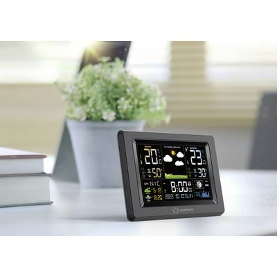 A digital weather station screen displays temperature, humidity, and weather forecast, with a plant in the background.