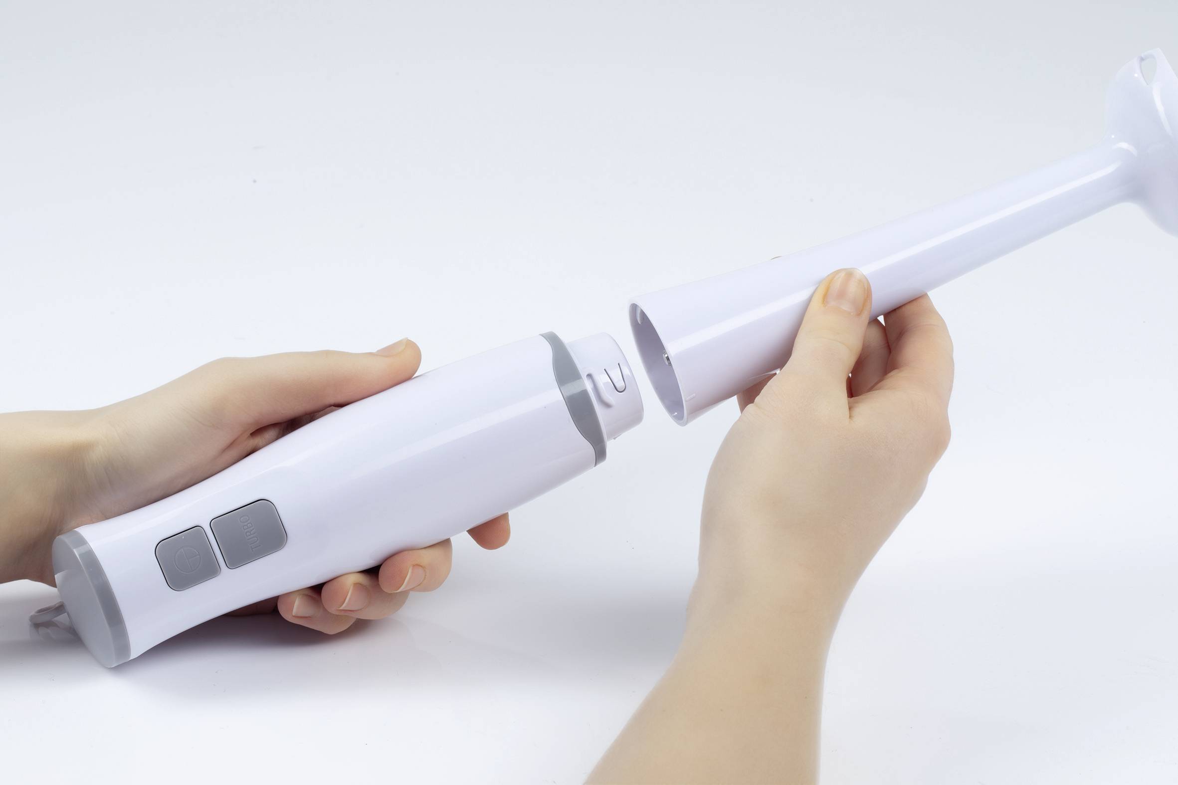 Two hands are assembling a white hand blender with dark grey buttons.