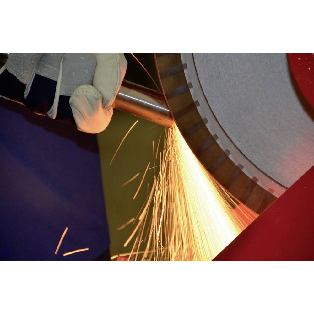 Worker cuts metal pipe with cutting disc, sparks flying. Protective gloves are visible, emphasising safety at work.