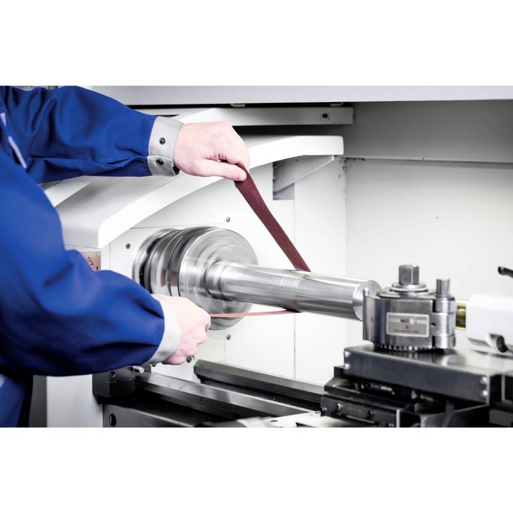 A person is using a grinding machine to polish a round metal component. The machine is located in a workshop environment.