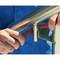 A person is sanding a metal handrail with an abrasive belt to smooth the surface. The hands and the handrail are in focus.