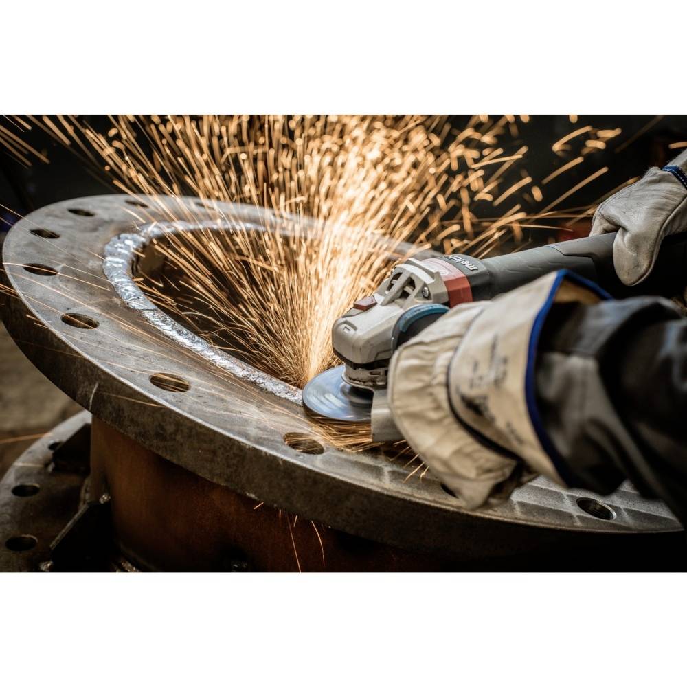 A person is grinding a large metal plate with an angle grinder, with sparks flying. They are wearing protective gloves.