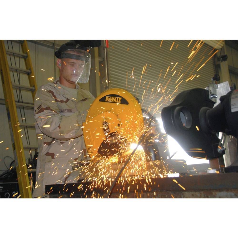 A soldier is wearing protective clothing and working in a workshop with an electric saw, with sparks flying.