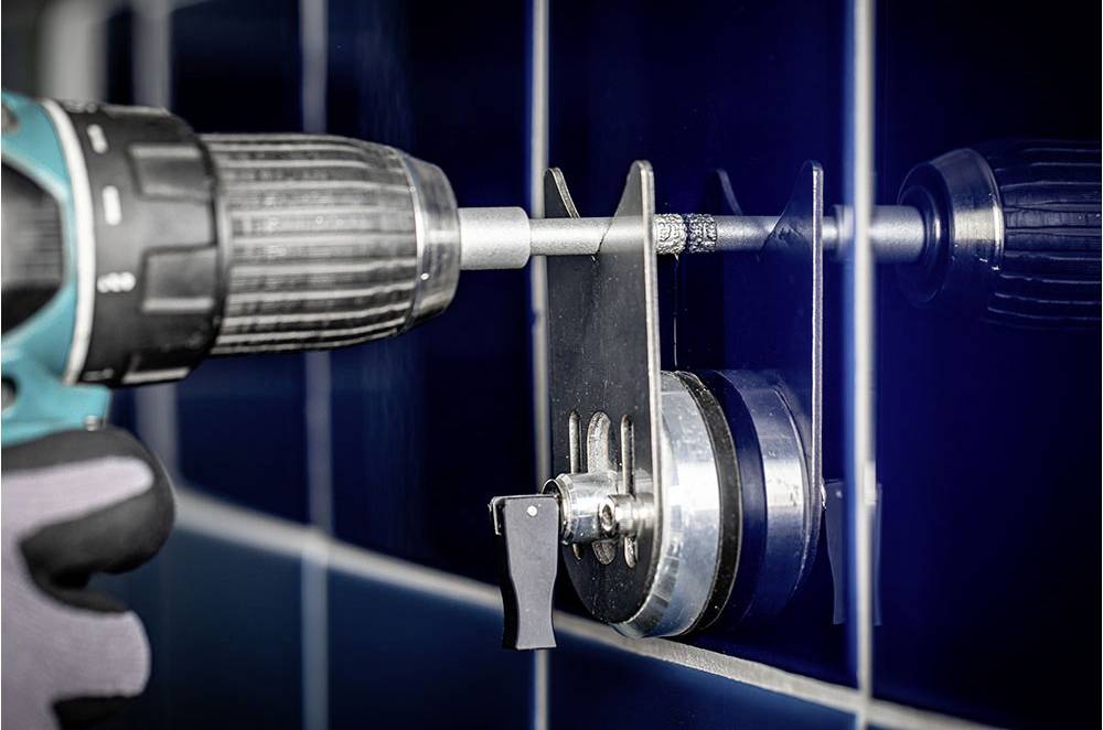 A person is using a drill with a special attachment to bore precise holes into a blue tiled wall.