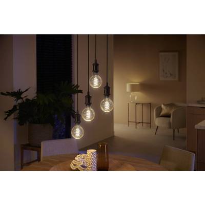 A cosily lit living room with four hanging light bulbs above a round wooden table. In the background are plants and furniture.