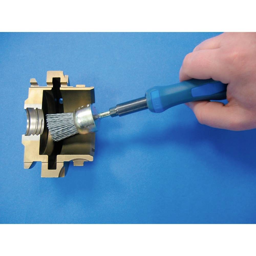 A hand holds a blue brush cleaning a metal surface within a gold-coloured metal part.