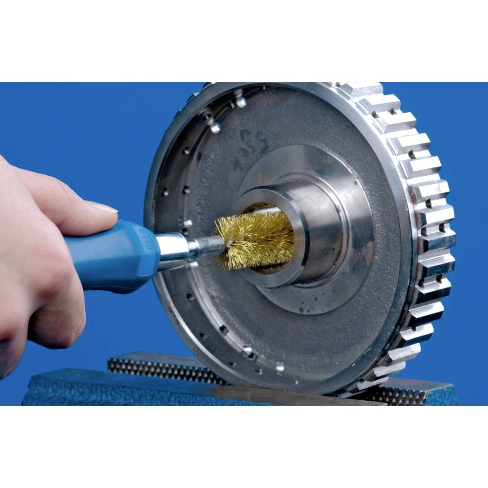A hand holds a blue tool with a wire brush, used for cleaning or polishing a metal gear wheel.