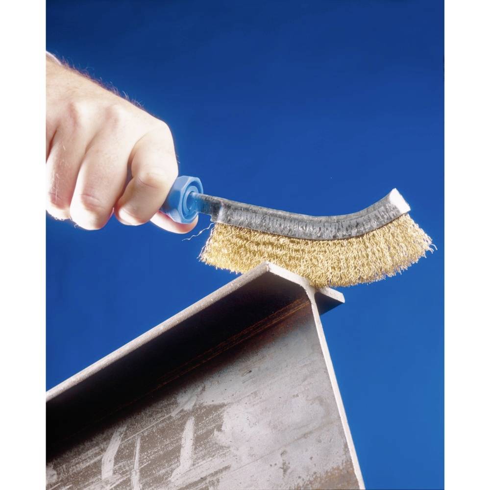 A hand holds a wire brush and cleans a metal surface. The background is blue.