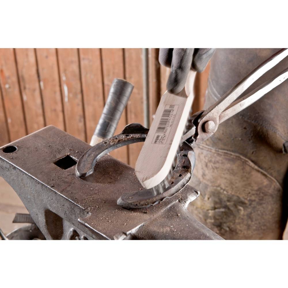 A person is shaping a horseshoe with a pair of tongs on an anvil. Hands are wearing protective gloves. Background of wooden planks.