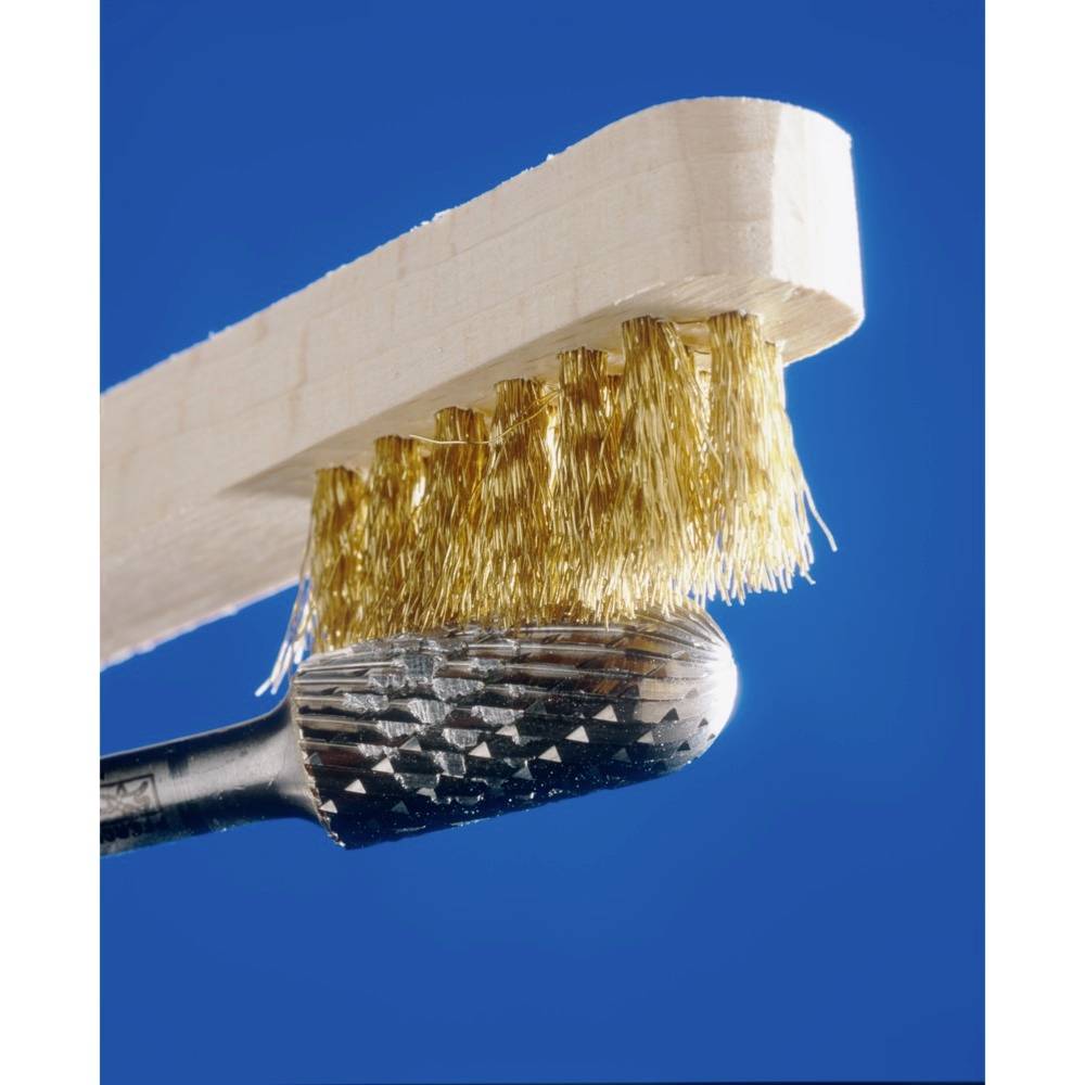 A wire brush cleans a piece of metal, creating clear lines on the surface against a blue background.