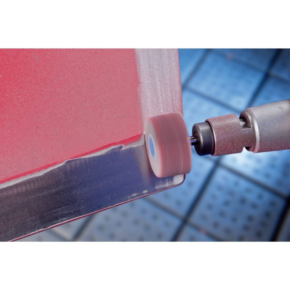 Close-up of a machine working on a red surface. Machine arm and grinding head visible, background blurred blue.