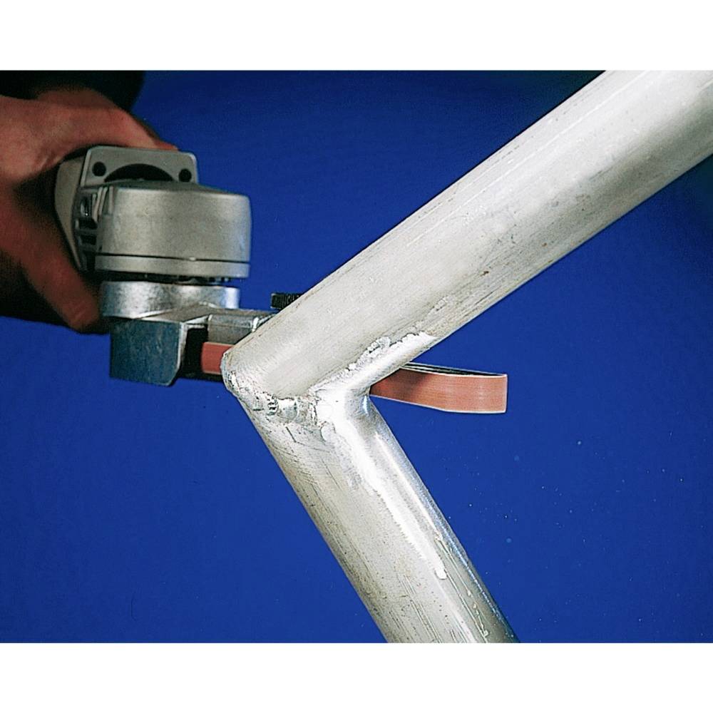 A person is grinding a metal weld at a frame corner with an angle grinder to smooth the surface.