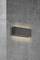 Modern wall light in rectangular form, mounted on a grey concrete wall. The light emits a warm, diffused glow.