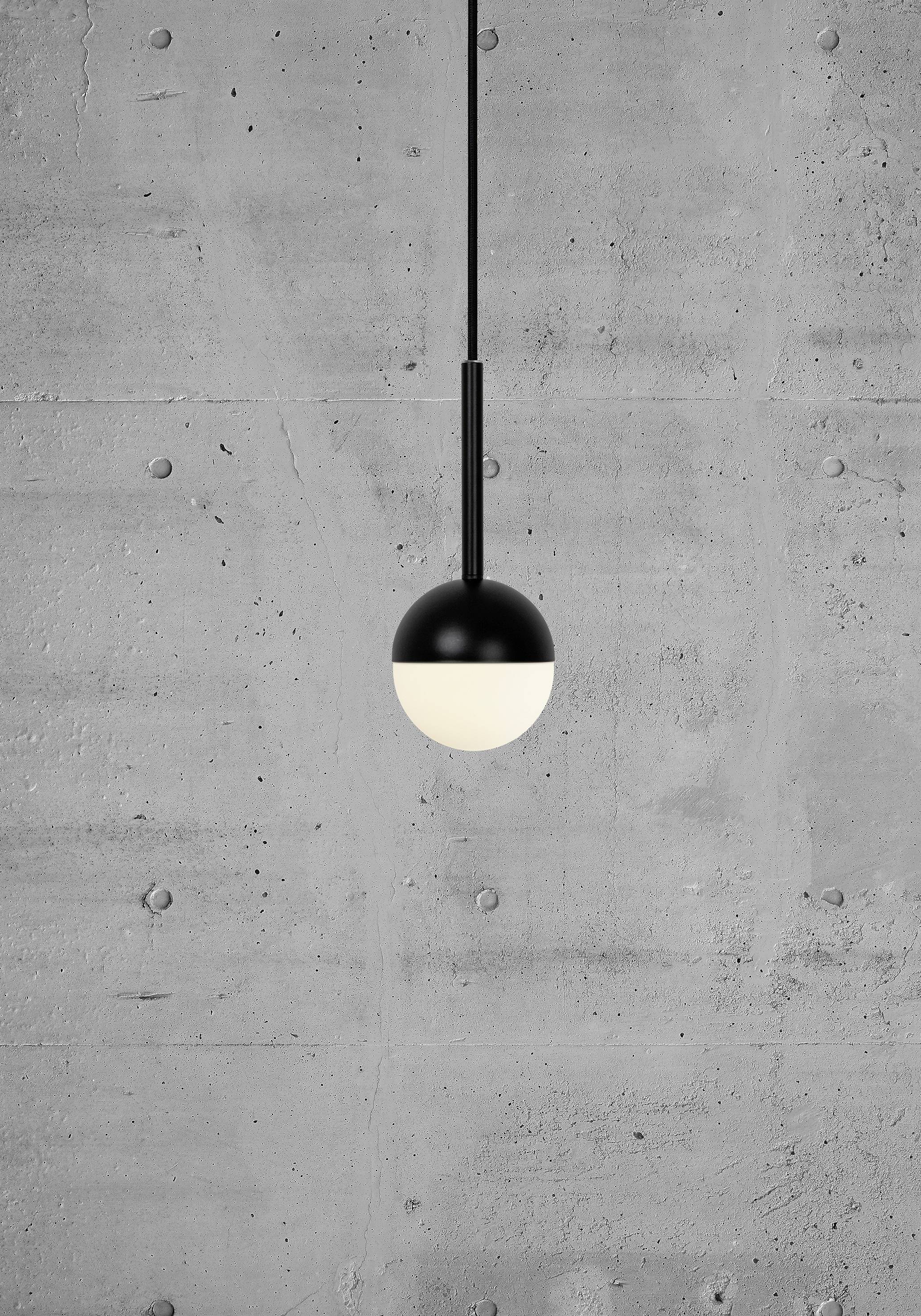 A modern pendant light with a round, two-tone design hangs in front of a grey concrete wall.