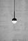 A modern pendant light with a round, two-tone design hangs in front of a grey concrete wall.