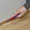 A hand cuts a piece of carpet with a craft knife along a floor covering.