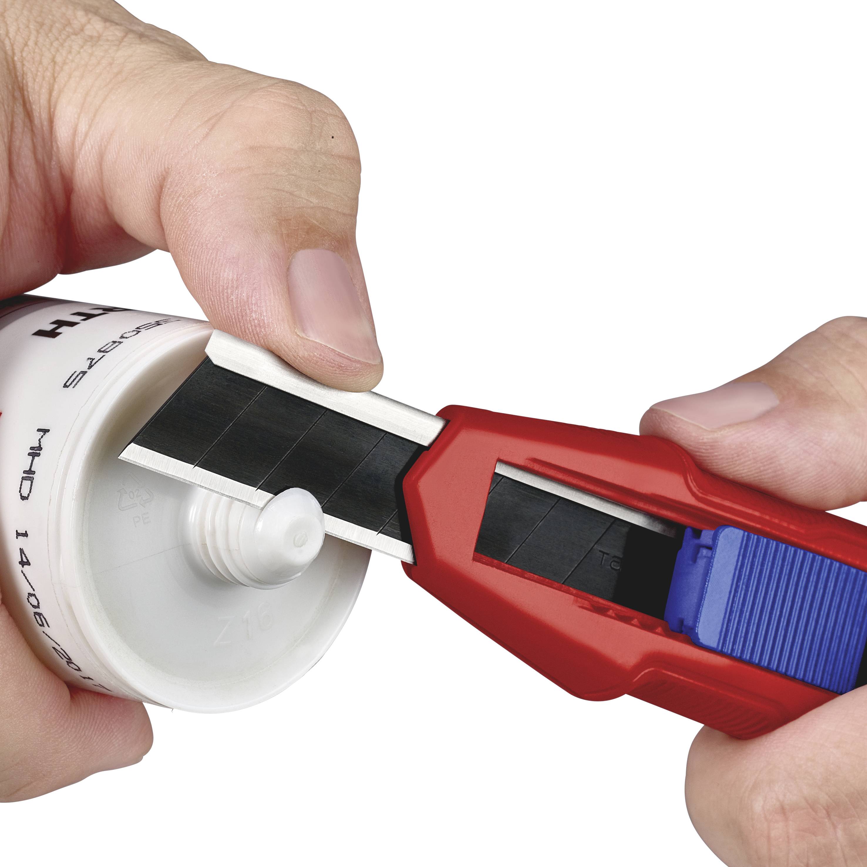 A person is cutting off the tip of a white plastic tube with a red utility knife.