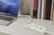 Laptop on a desk beside a multi-socket extension lead and earphones. Books are standing in the background.