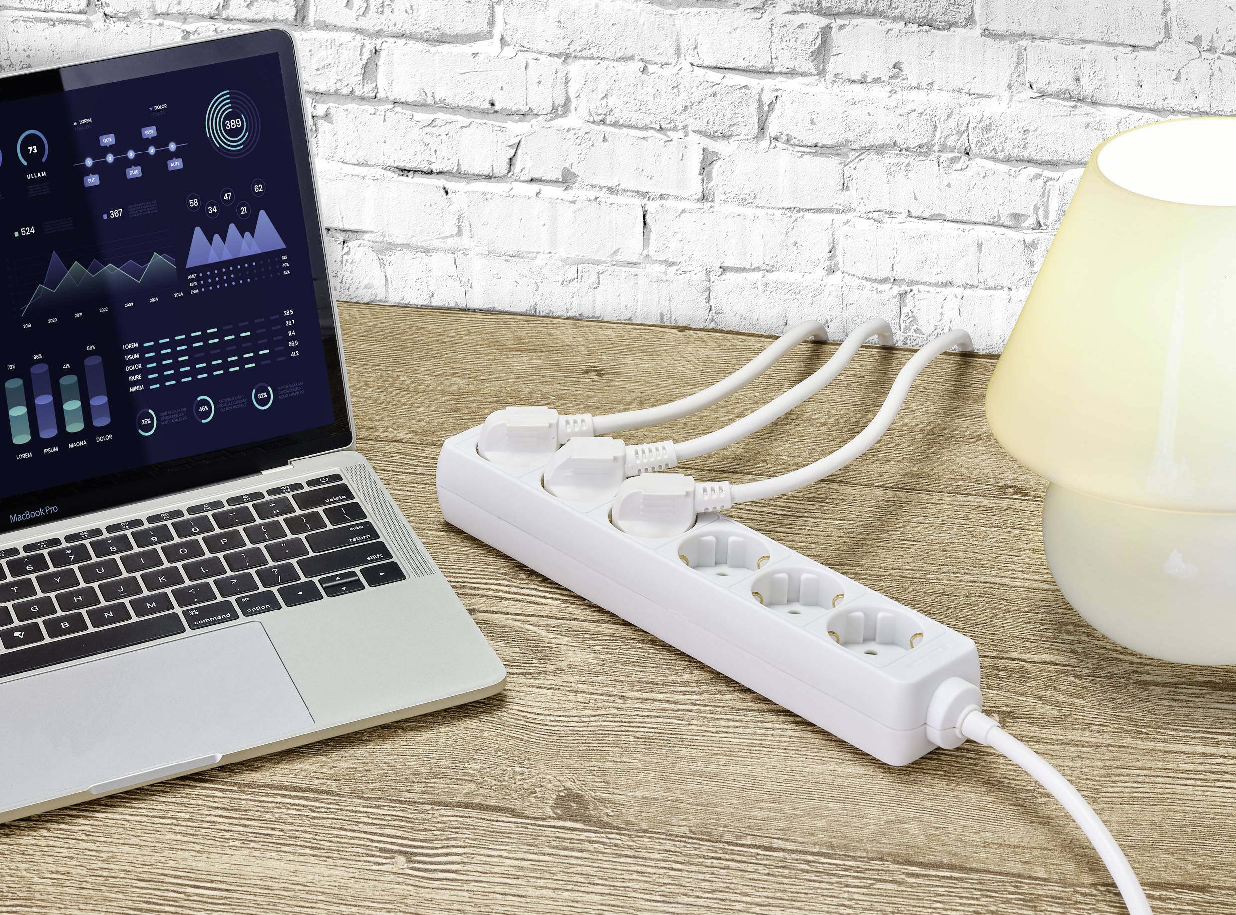 A laptop with diagrams on the screen sits on a table next to a white multi-socket extension lead and a desk lamp.