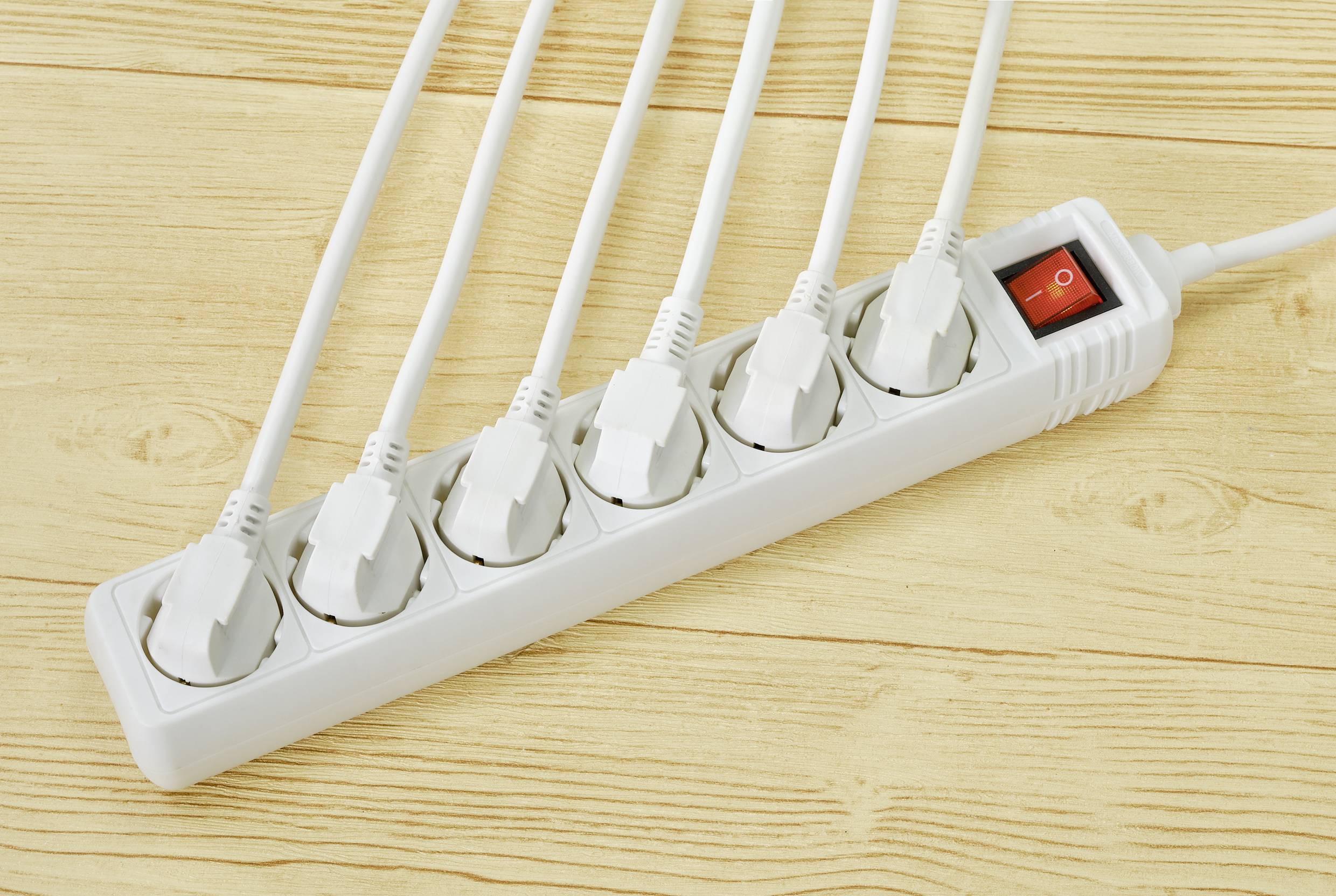 Six-way extension socket with switch, all sockets in use. Resting on a wooden surface.