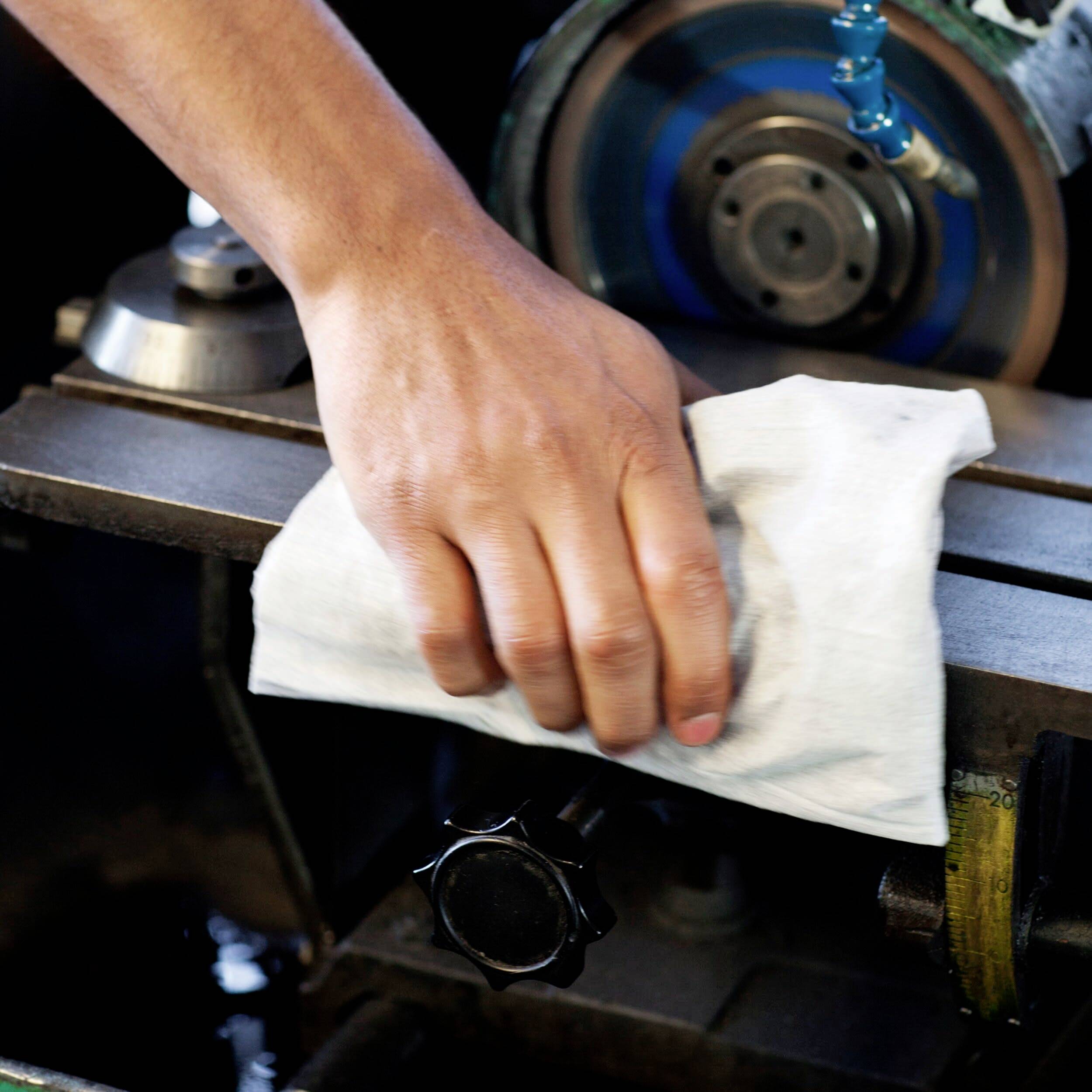 A hand is cleaning a metal machine in a workshop with a white cloth to ensure cleanliness and maintenance.