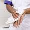 A person with brown skin is drying their wet hands with a white paper towel in a room with white tiles.