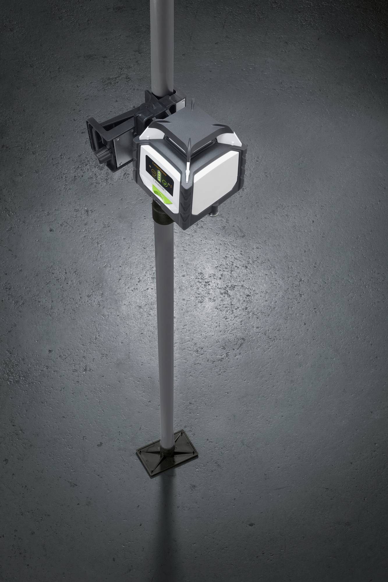 A laser levelling device is mounted on a tripod. It is illuminated and projects a green laser beam vertically onto the floor.