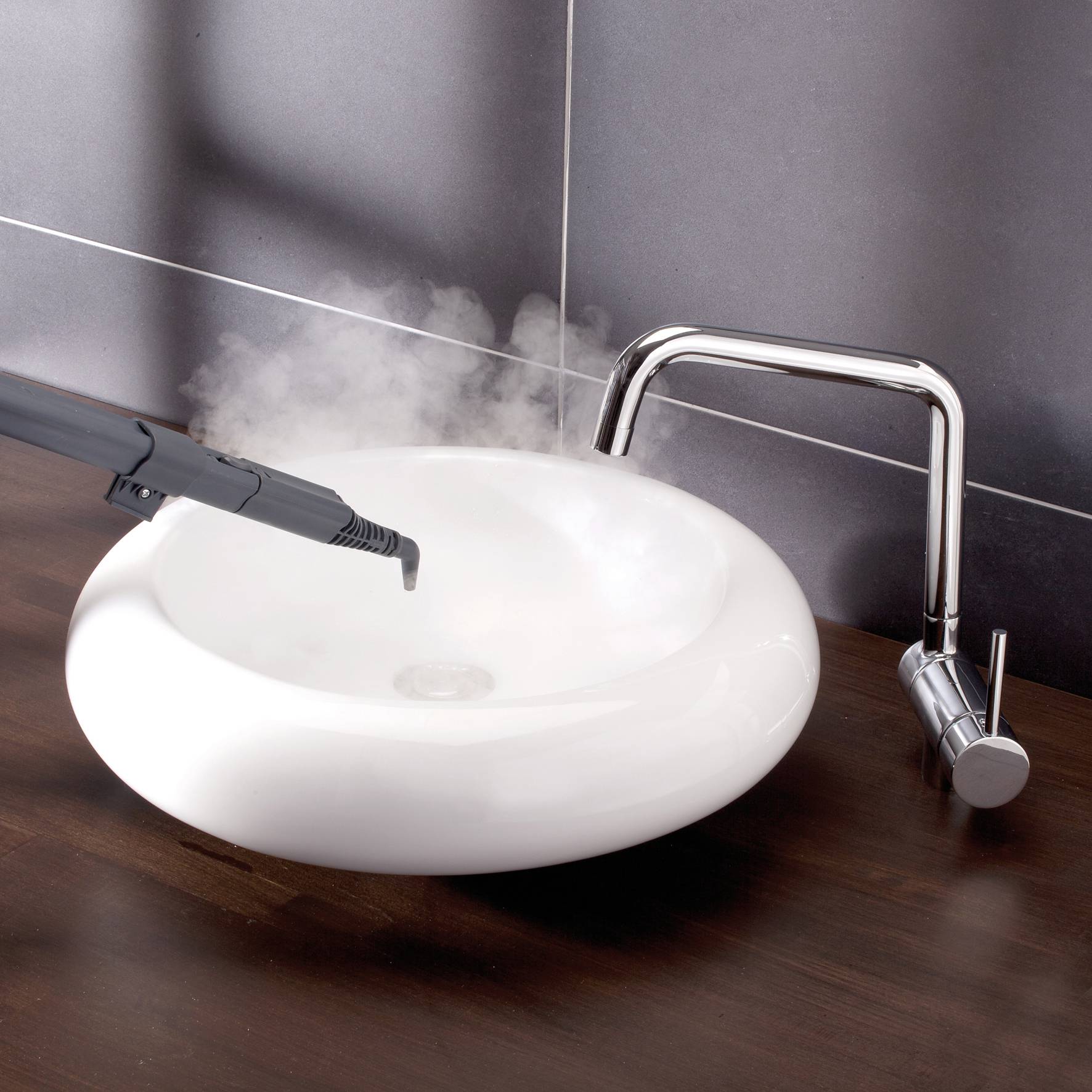 A steam cleaner is directed at a white sink, with steam rising above the basin; focus on cleaning.