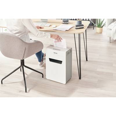 A person is sitting at a desk, feeding a sheet of paper into a shredder, with office supplies in the background.