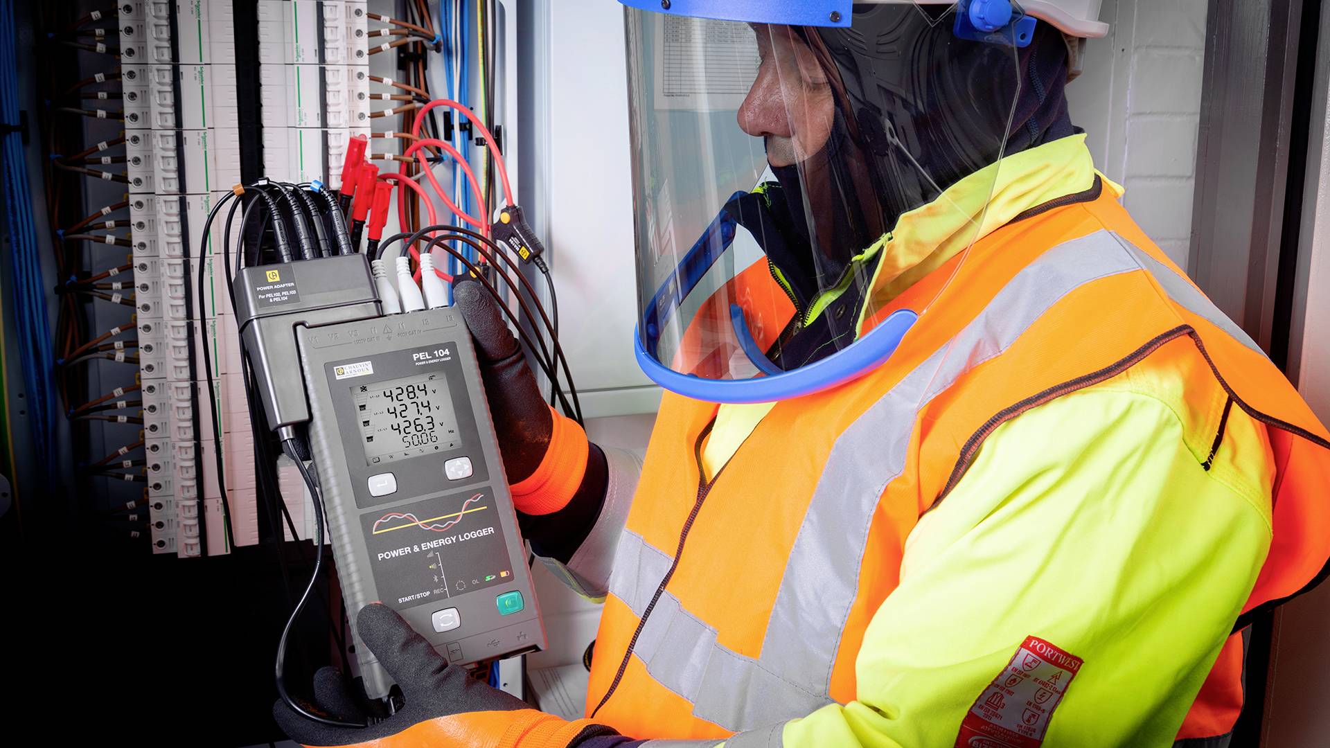 A person in protective clothing is checking electrical cables with a digital measuring device in an electrical cabinet.