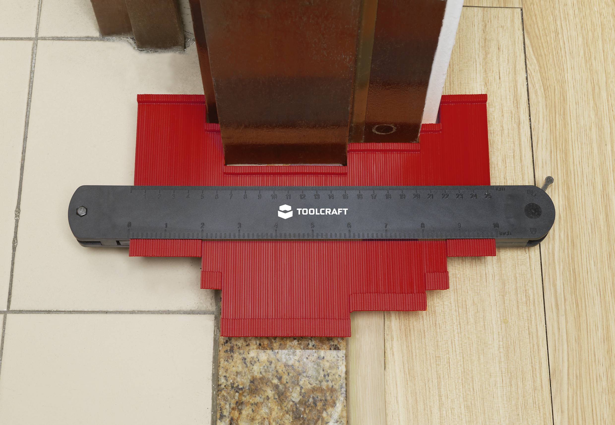 A red contour gauge knife curves around a room corner with various floor coverings to measure the contours.