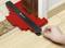 A person is using a red contour gauge tool to measure the shape of a door threshold on a light wooden floor.