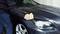 A person is cleaning the bonnet of a car with a yellow cloth. The car is dark and is parked in a garage.
