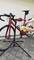 A person is cleaning a red racing bicycle on a bike stand with a yellow cloth and a spray bottle.
