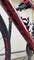 A red racing bicycle is standing on a bike rack in front of a white wall.