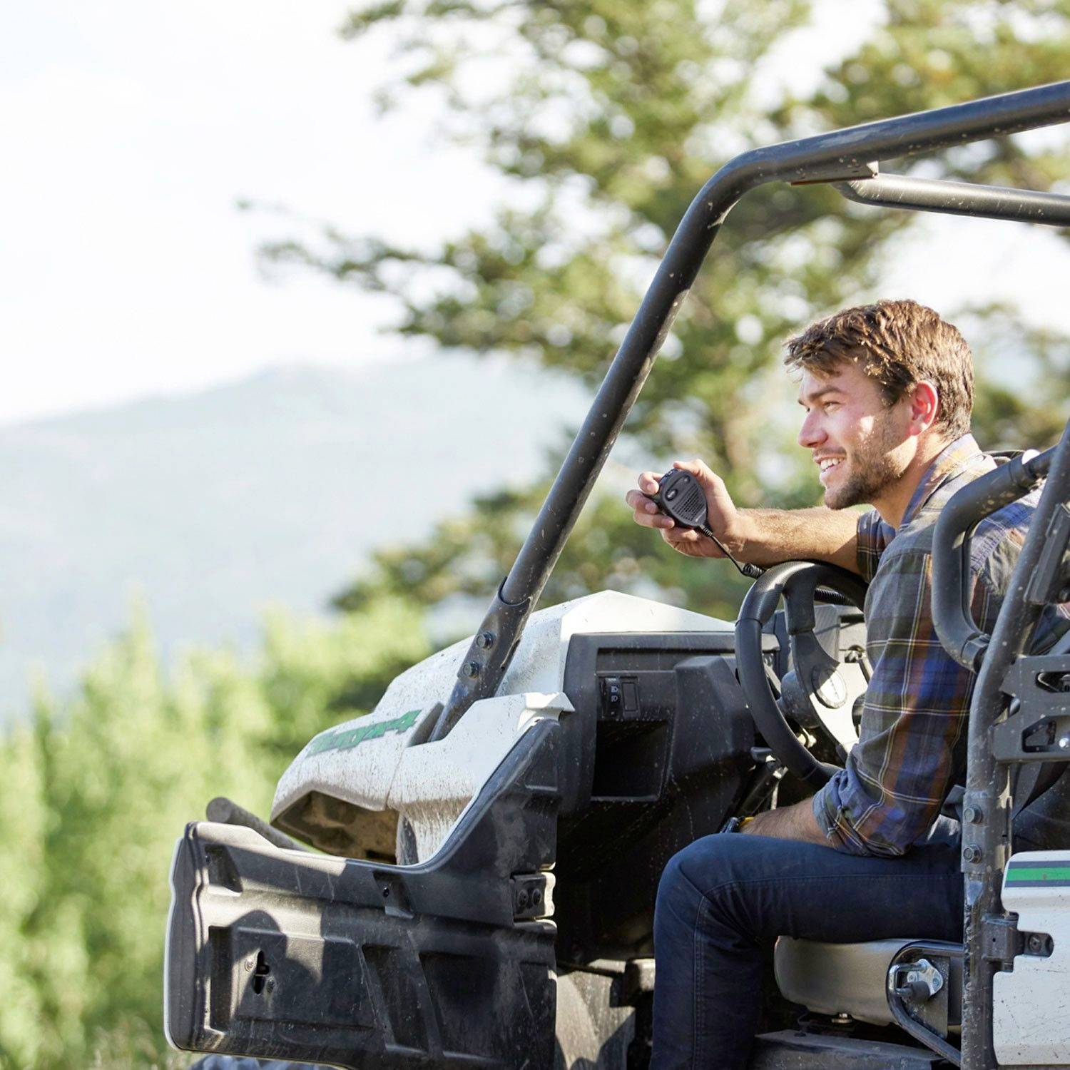 A man is sitting cheerfully in an off-road vehicle, holding a mug, and is in a rural, green setting.