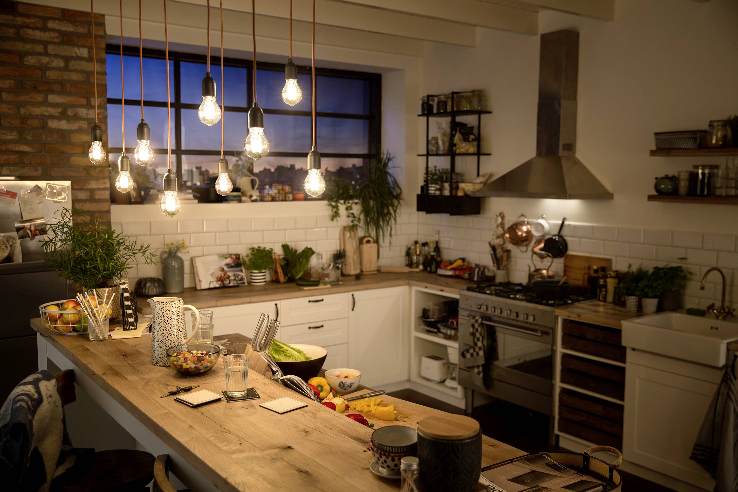 Cosy kitchen with hanging light bulbs, wooden worktops and modern equipment, including cooker, sink and kitchen utensils.
