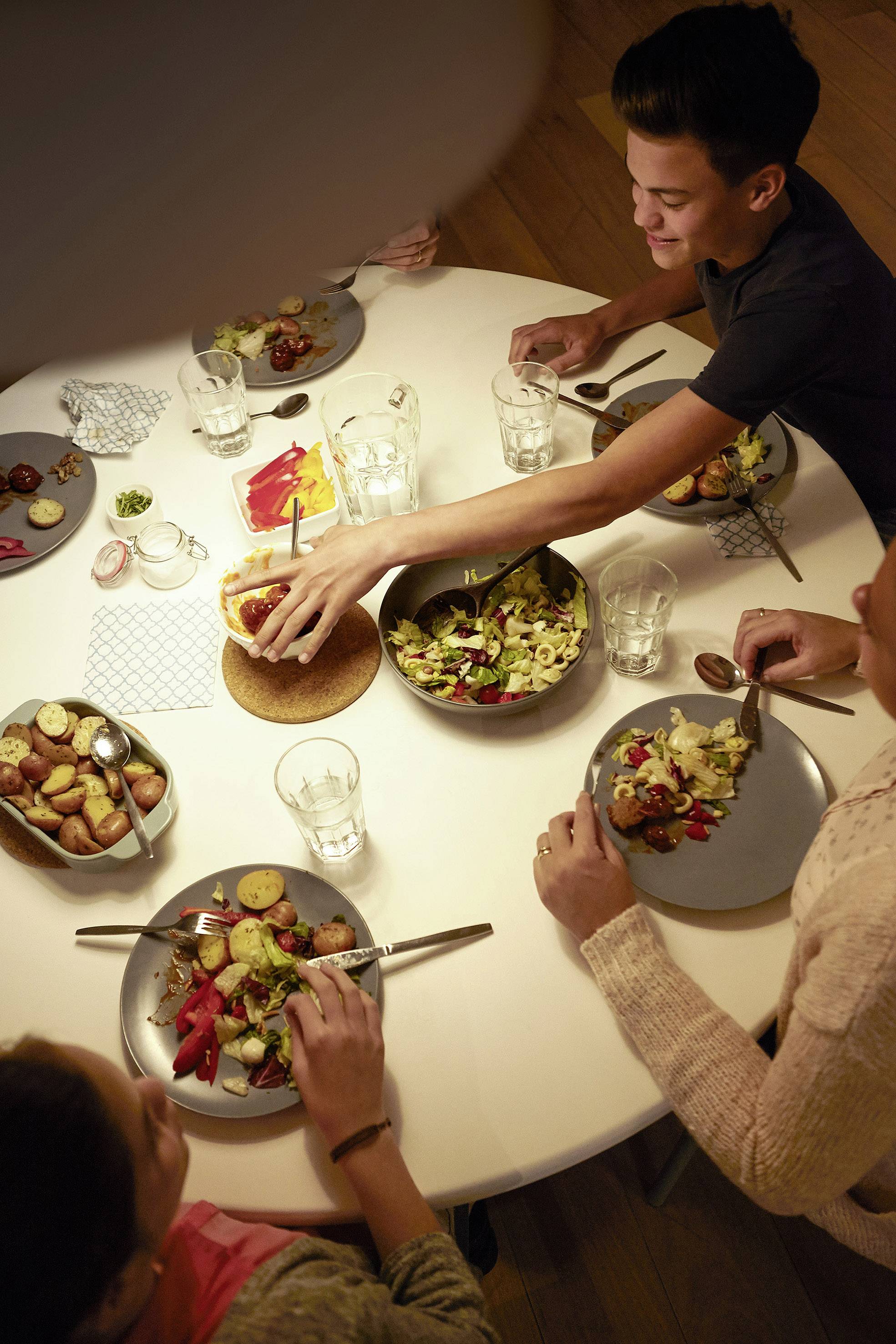A group of people are sitting around a table and eating together. On the table are salads, bread and drinks.