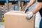 A person opens a large cardboard box with a utility knife in a warehouse, surrounded by shelves full of additional parcels and boxes.