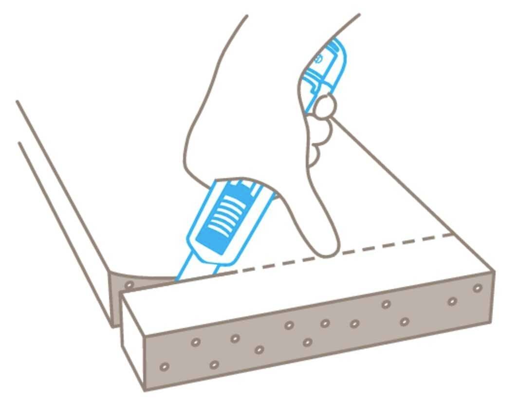 A hand uses a blue glue gun to apply adhesive along a dotted line on wood.