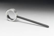 A metal ring is connected to a long, thin rod. The ensemble is resting on a light surface with a dark background.