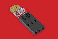 A black electric adapter or connector with multiple socket slots lies on a red background.