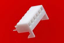 A white plastic plug with six connection sockets against a red background. The plug is white and slightly angled.