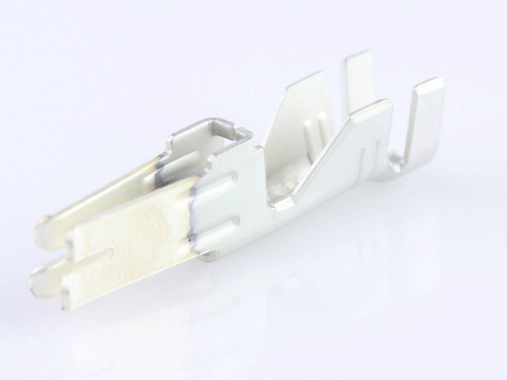 A metallic plug contact with hooks and slots, used in electrical connections, is lying on a white surface.