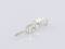 A small, silver metal pin with a complex shape lies on a white surface, slightly reflecting light.