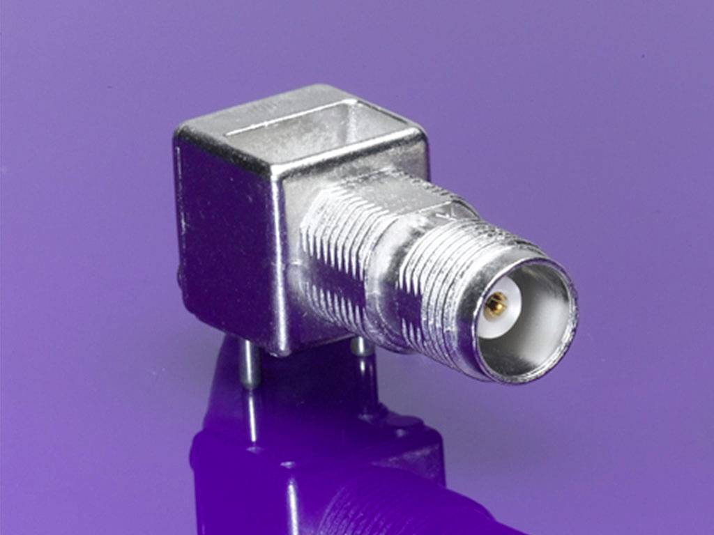 A silver coaxial plug with a square housing on a purple background, suitable for electronic connections.