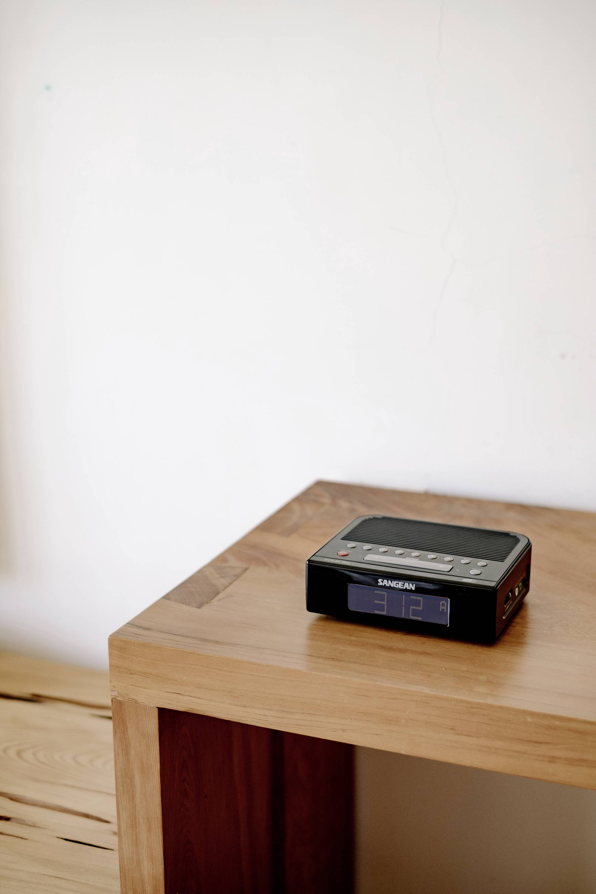 A black, rectangular radio sits on a wooden table in front of a white wall.